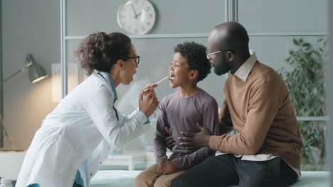 Female-Doctor-Checking-Throat-of-African-American-Boy-with-Flashlight